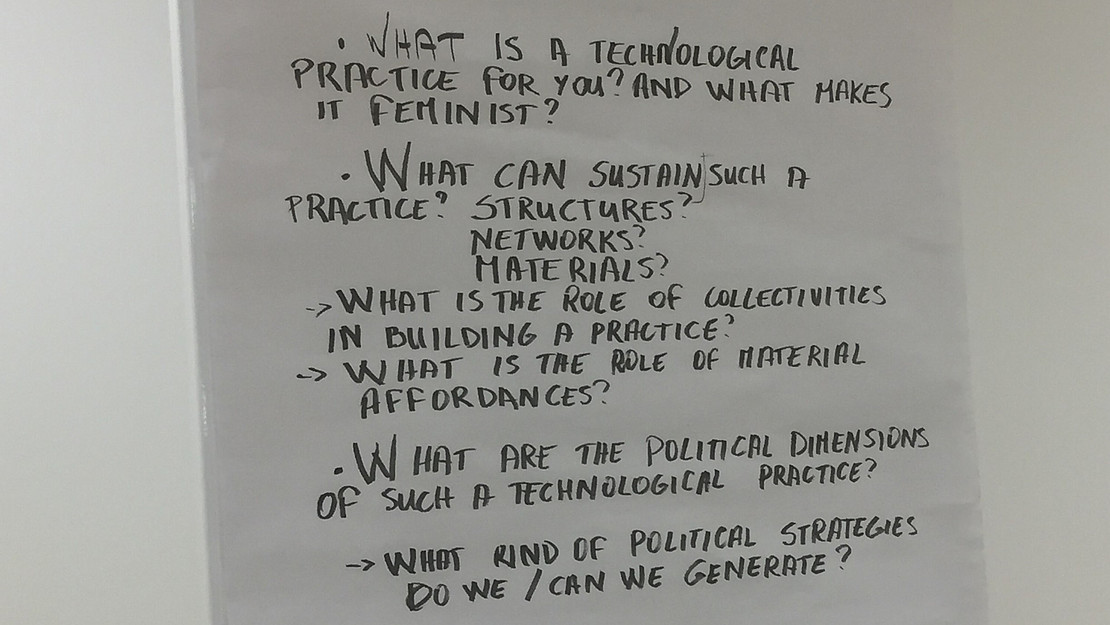 Written text on a flipchart: "What is a technological practice for you? And what makes it feminist?; What can sustain such a practice? Structures? Networks? Materials? What is the role of collectivities in building a practice? What is the role of material affordances?; What are the political dimensions of such a technological practice? What kind of political strategies do we / can we generate?"
