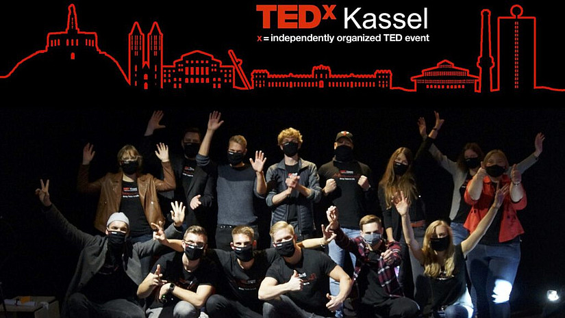 Gruppenbild: Die Veranstaltenden der TEDx Kassel sind vor einem schwarzen Hintergrund versammelt. Auf dem Hintergrund ist das Logo der TedX Kassel zu sehen. 