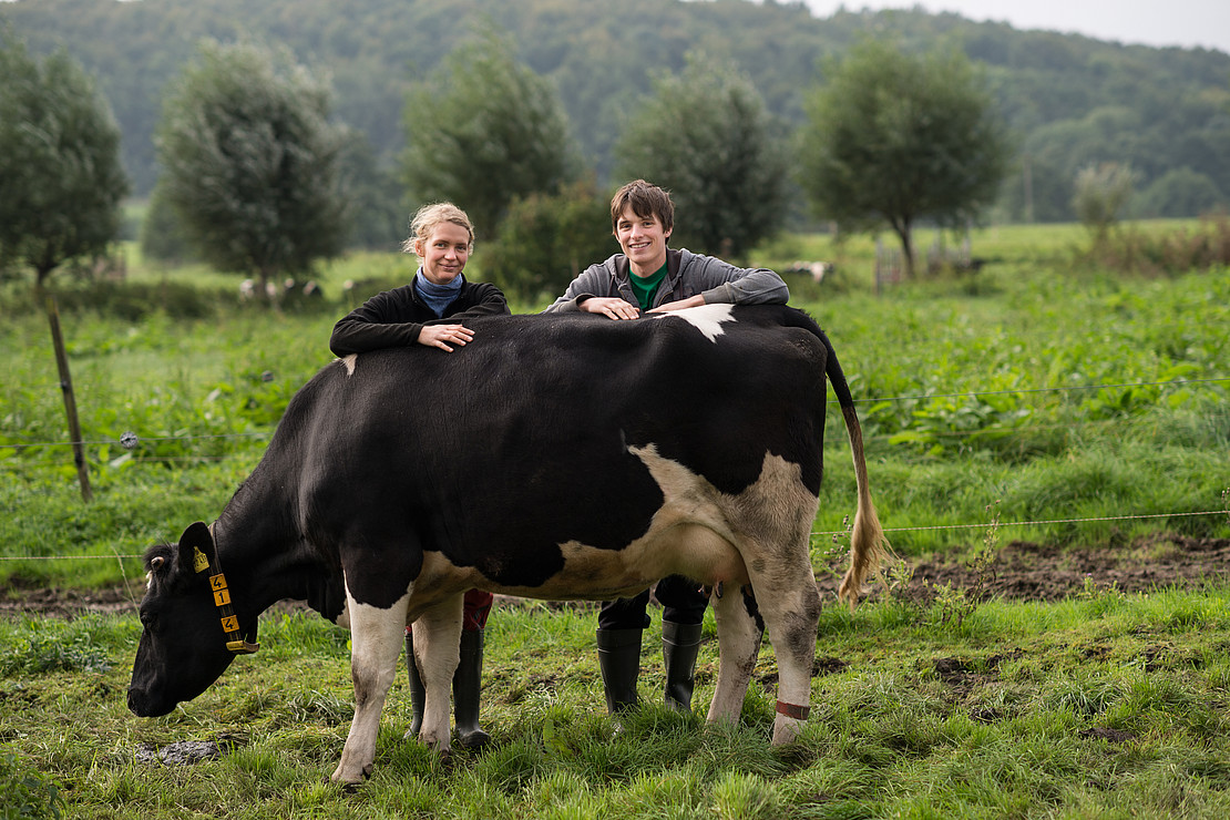 Two students lean against a cow and look into the camera