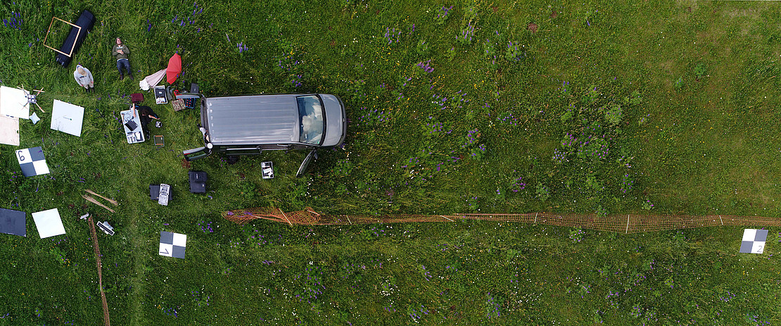 Drone image from 10 m height showing grassland and unpacked sensor equipment distributed around a bus