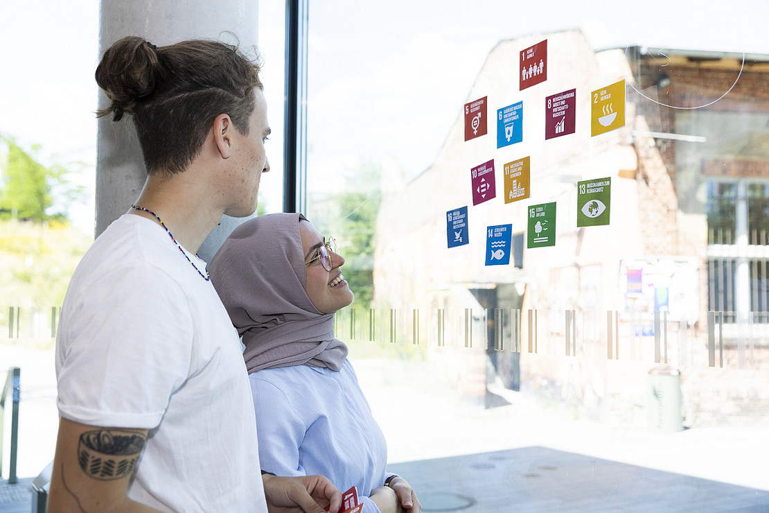 Two people look at a window on which the SDGs are stuck as stickers