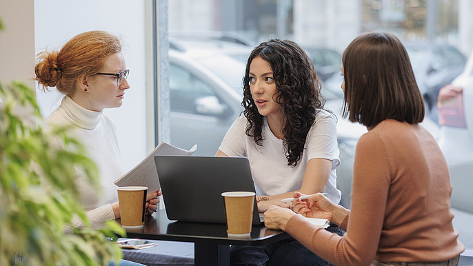 3 Frauen im Gespräch am Tisch mit Laptop