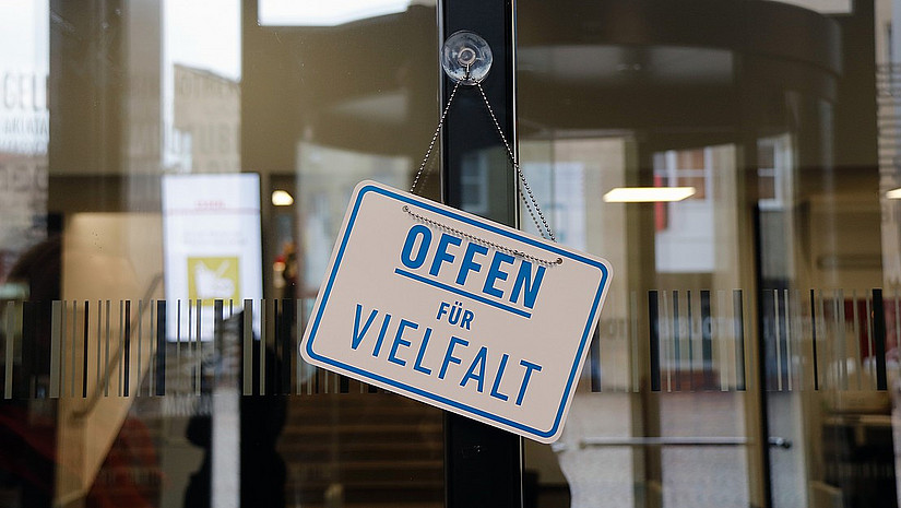 Foto eines Türschilds mit dem Schriftzug "Offen für Vielfalt" an der Glastür der Bibliothek Holländischer Platz.