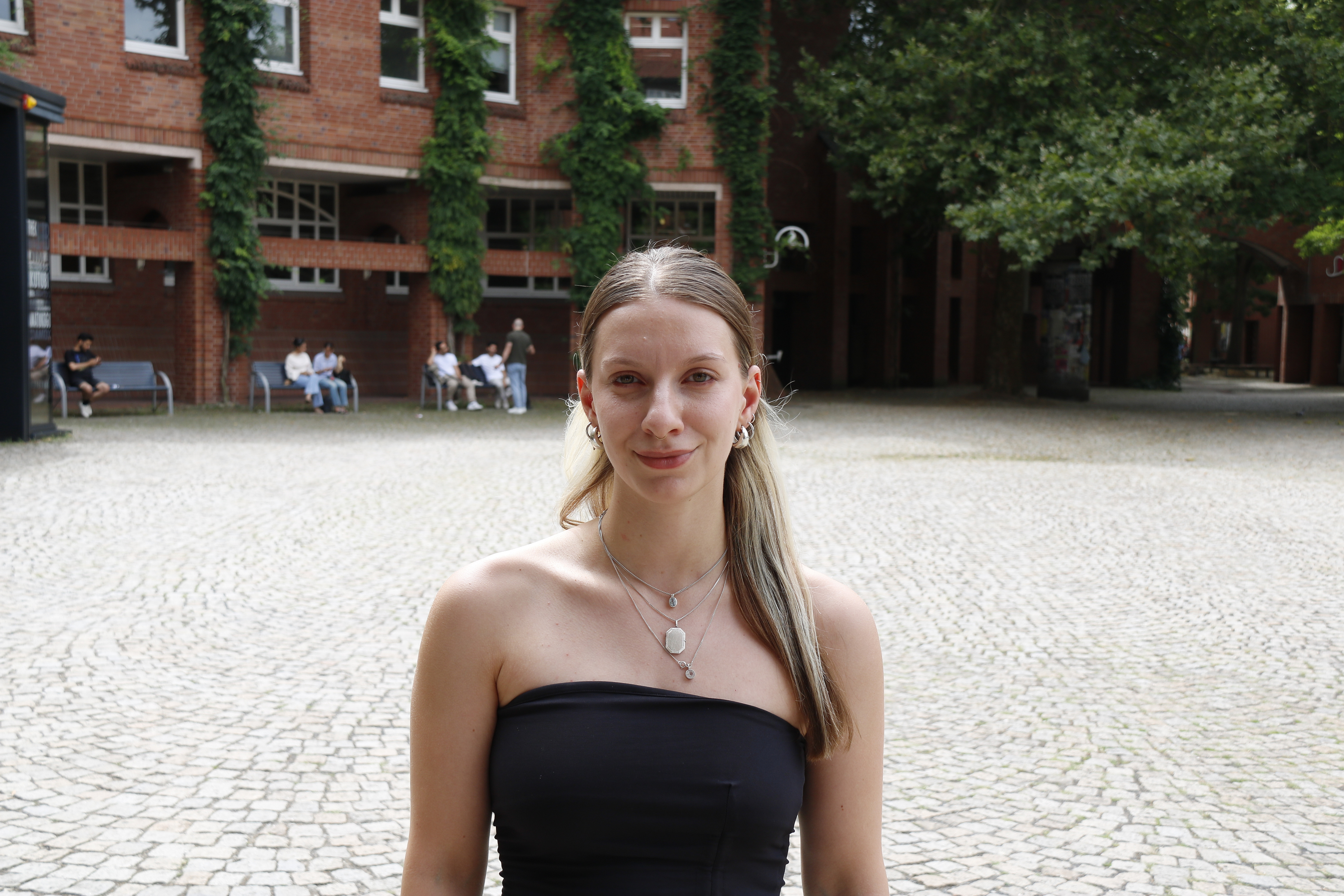 Junge Frau blickt in die Kamera im Hintergrund die Univeritätsbibliothek der Uni Kassel