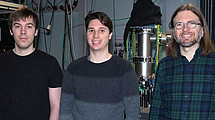 Das Foto zeigt Die Kasseler Physiker Fabian Westmeier, Nicolas Ladda, Arne Senftleben vor ihrer experimentellen Apparatur