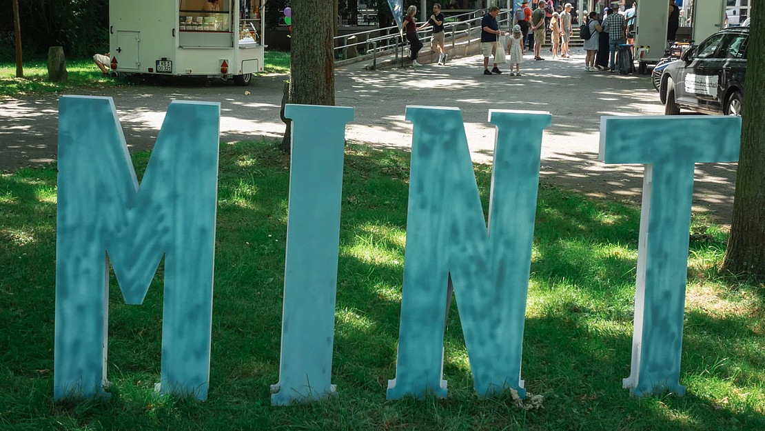 mintfarben gestrichene Buchstaben M I N T auf Rasen vor einem Gebäude aufgestellt
