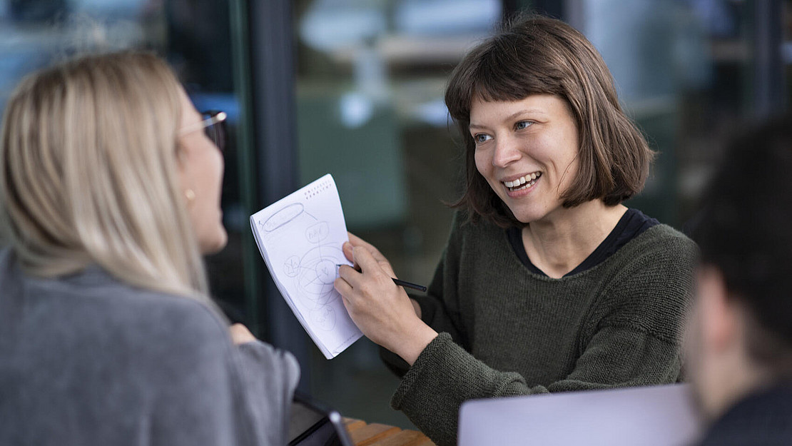 Zwei Frauen im Gespräch, eine Frau hält einen Zettel in der Hand
