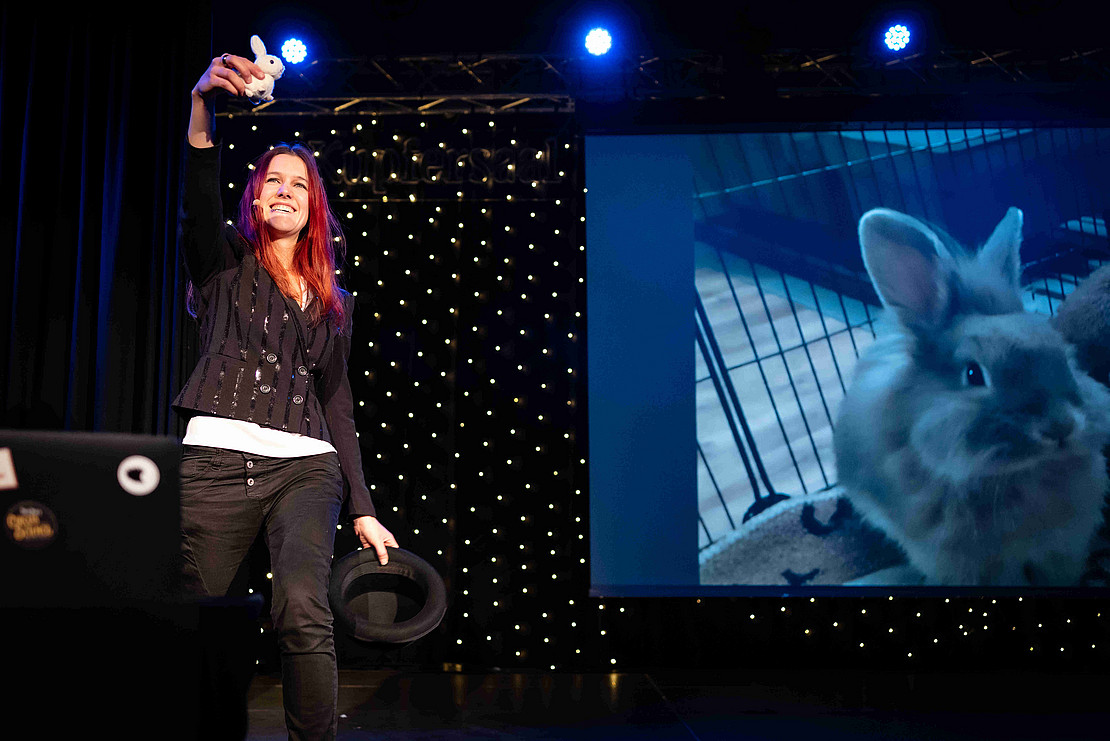 Patsch auf der Bühne hält einen Plüschhasen in der einen und einen Zylinder in der anderen Hand.