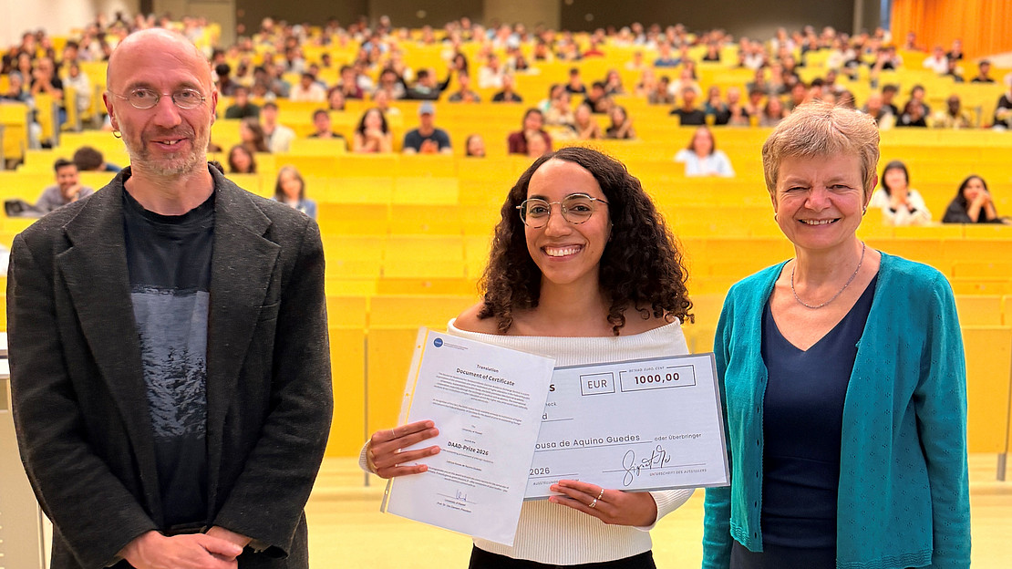 Universitätspräsidentin Prof. Dr. Ute Clement (rechts) und Prof. Dr. Aram Ziai, Programmdirektor des Masterstudiengangs Global Political Economy and Development (links), gratulieren Letícya Sousa de Aquino Guedes zur Auszeichnung mit dem DAAD-Preis 2026.