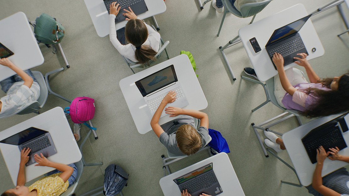 Schüler:innen sitzen an Tischen und bedienen ihre Laptops.