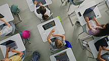 Schüler:innen sitzen an Tischen und bedienen ihre Laptops.