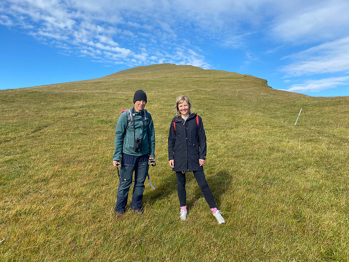 Two smiling people on a green meadow against a blue background