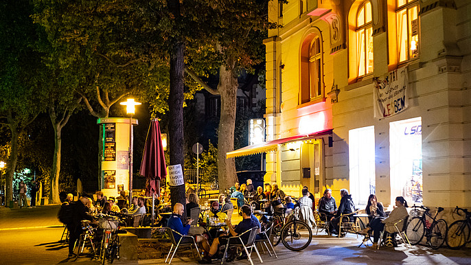 Das Bild zeigt Menschen, die abends vor einer Bar im Vorderen Westen zusammensitzen.
